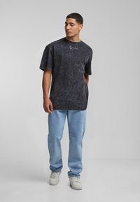 Black marbled oversized t-shirt with short sleeves and a crew neckline, paired with light blue jeans and white sneakers.