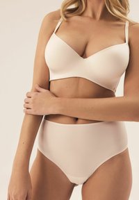 Jasbeżowy biustonosz z gładkimi, formowanymi miseczkami i regulowanymi ramiączkami, w połączeniu z jasbeżowymi wysokimi majtkami, oba wykonane z miękkiego, elastycznego materiału.