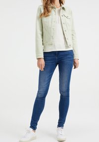 Vihreä denimi-takki, valkoinen neulepusero ja tummansiniset tiukat farkut yhdistettynä valkoisiin lenkkareihin. Rakenteellinen kangas ja istuva malli.