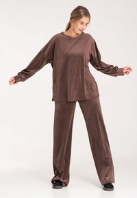 Brązowy zestaw odzieży do relaksu wykonany z miękkiego, aksamitnego materiału. Bluzka z długim rękawem o luźnym kroju i dopasowane szerokie spodnie. Gładka faktura na całej powierzchni.