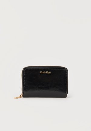 Czarny portfel Calvin Klein zapinany na zamek z złotym logo i suwakiem, pokazany zamknięty na gładkim białym tle.