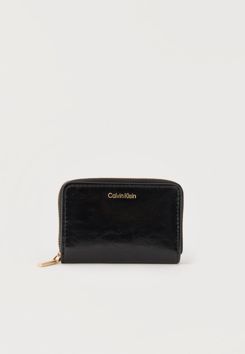 Μαύρο πορτοφόλι Calvin Klein με φερμουάρ γύρω γύρω, με χρυσό λογότυπο και τράβηγμα φερμουάρ, απεικονίζεται κλειστό σε απλό λευκό φόντο.