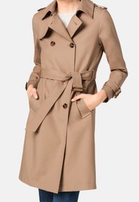 Trench coat beige in tessuto liscio, con design doppiopetto, cintura in vita e tasche laterali. Colletto dritto e dettagli con bottoni.