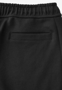 Zwarte joggingsbroek met een gladde textuur, voorzien van een platte achterzak en een elastische tailleband zonder extra versieringen.