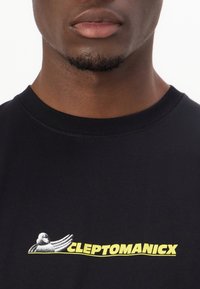 Black cotton t-shirt featuring a graphic of a duck and the text "CLEPTOMANICX" in bold yellow letters, crew neckline, and short sleeves.