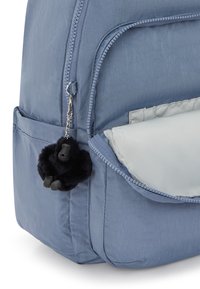 Světle modrý batoh s částečně otevřenou přední kapsou a malým černým plyšovým klíčením ve tvaru gorily připevněným k zipu.