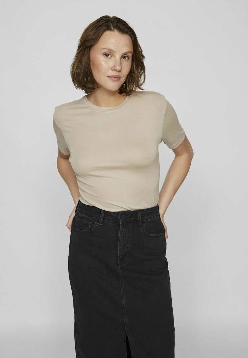 Beige short-sleeve top paired with a high-waisted black denim skirt featuring a front slit. Smooth texture and fitted design.