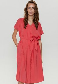Rochie coral cu decolteu în V, mâneci scurte și un brat dinălțime la talie. Construită dintr-un material neted, ușor, cu o croială confortabilă.
