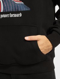 Sort sweatshirt med en frontlomme, der har et grafisk design og teksten "power forward." Stoffet er struktureret og ribbet ved ærmerne.