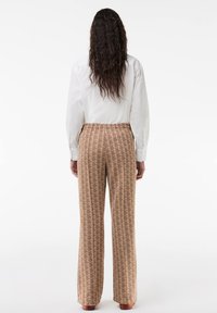 Brown patterned trousers with a relaxed fit and elastic waistband, paired with a white long-sleeve shirt, viewed from the back.
