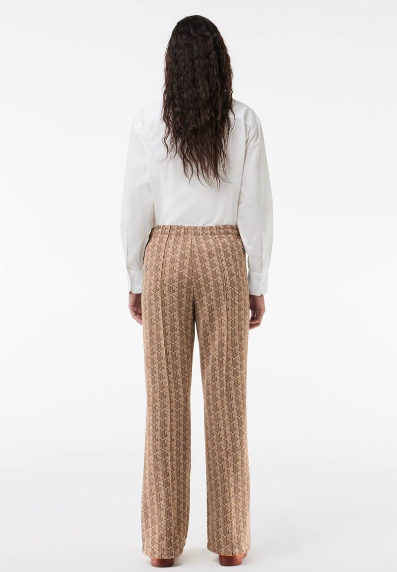 Brązowe spodnie w wzory o luźnym kroju i elastycznym pasku, połączone z białą koszulą z długim rękawem, widok z tyłu.