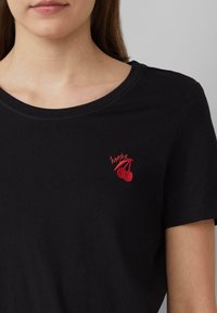 Zwarte katoenen t-shirt met een ronde halslijn. Voorzien van een rode geborduurde kers graphic op de linker borst. Korte mouwen.