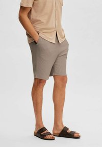 Chemise beige à boutons, short à rayures beige, et sandales à glissière marron. Le short dispose de poches latérales et d'un tissu lisse et léger.