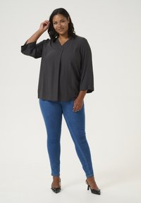 Blouse noire texturée avec un décolleté en V et des manches trois-quarts, assortie à un jean skinny bleu et des escarpins noirs à bout pointu.