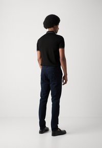 Polo noir avec des finitions contrastées, pantalon bleu marine et chaussures noires. La chemise a un col classique et des manches courtes.