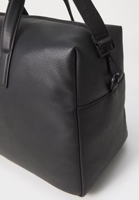 Sac en faux cuir noir avec une finition texturée, de forme rectangulaire et à poignées courtes. Dispose d'une bandoulière amovible et d'un design minimaliste.
