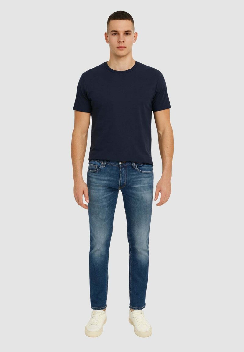 Marineblauwe T-shirt met korte mouwen, gecombineerd met lichtblauwe slim-fit jeans. Model draagt witte sneakers. Eenvoudig ontwerp en effen kleuren.