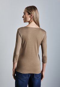 Maglietta beige a maniche lunghe con scollatura rotonda e maniche aderenti, abbinata a jeans blu scuro. Tessuto liscio con una leggera lucentezza.