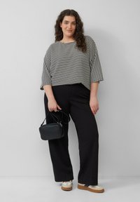 Zwart-wit gestreept cropped top met 3/4 mouwen, gecombineerd met zwarte wijde broek en een kleine zwarte handtas. Sneakers met een dikke zool.