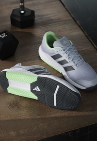 Chaussures de course Adidas grises et vertes sur un sol en bois à côté de deux haltères noirs de 25 livres.