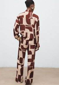 Braun und beige gemustertes Outfit bestehend aus einem lockeren Hemd und weitem Hosenbein, gefertigt aus glattem Stoff mit abstrakten Formen und Akzenten.
