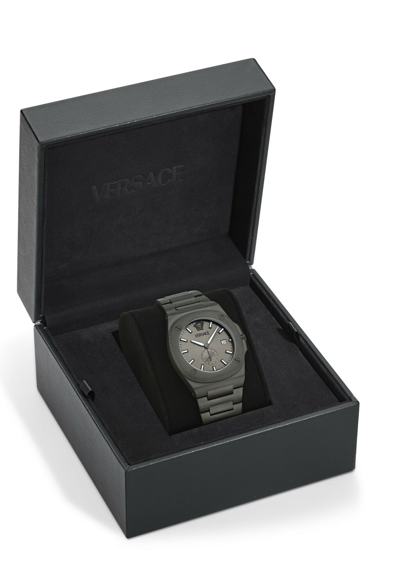 Versace-horloge in een zwarte doos met een plush interieur. De horloge is grijs met een gestructureerde band, een ronde wijzerplaat en zilveren accenten.