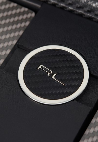Black leather detail featuring a circular carbon fiber emblem with the letters "RL" in silver, set against a textured material backdrop.
