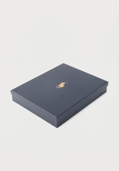 Boîte rectangulaire bleu marine avec un logo joueur de polo doré centré sur le couvercle, fermé et posé sur une surface blanche.