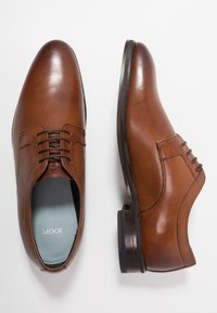 Chaussures habillées en cuir marron avec une finition lisse, un bout rond et des détails de couture subtils. Présentent un laçage traditionnel à œillets et un petit talon.