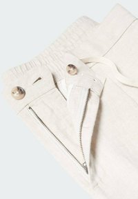 Pantalon en lin beige avec une taille élastique, doté d'une fermeture éclair à l'avant et de deux boutons ronds. Tissu texturé avec une finition lisse.