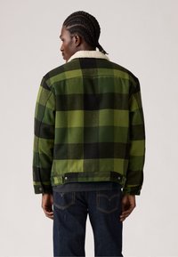Chaqueta de cuadros verde y negra con un cuello de borreguito, hecha de un tejido texturizado, que presenta un diseño corto y cierres de botones a presión.