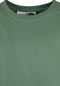 Camiseta de cuello redondo verde de Urban Classics que muestra el cuello y la etiqueta de la marca con advertencia de cuidado en el interior del cuello.