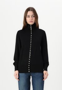 Maglione nero a maglia con colletto alto, caratterizzato da una linea centrale di bottoni argentati lucidi, maniche lunghe e una vestibilità aderente.