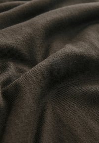 Sötétbarna szövet, amely puha tapintású, sima, kötött mintával rendelkezik, és finom vastagságbeli eltérések jellemzik az anyagon.