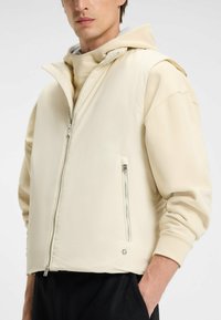 Giacca cappuccio beige con zip frontale, polsini a coste e dettagli in zip argentata. Realizzata in tessuto morbido e leggero con una vestibilità rilassata.