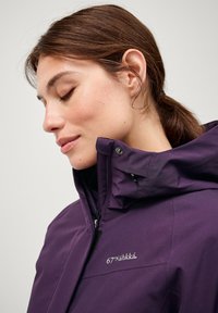 Lila wasserdichte Jacke mit hohem Kragen, Reißverschluss und Logodetail. Sie verfügt über eine glatte Textur und verstellbare Elemente an der Kapuze.