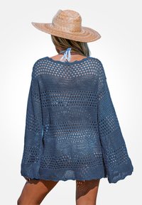 Cover-up all'uncinetto di colore blu navy con motivo a rete, maniche lunghe e orlo ondulato. Abbinato a un cappello di paglia con nastro.