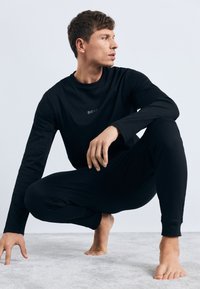 Conjunto de ropa de descanso negro que incluye una camiseta de manga larga con cuello redondo y logotipo, combinada con pantalones ajustados, fabricados en un tejido suave y liso.