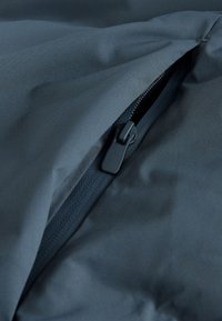 Black fabric with a partially unzipped black waterproof zipper and black zipper slider visible in close-up.