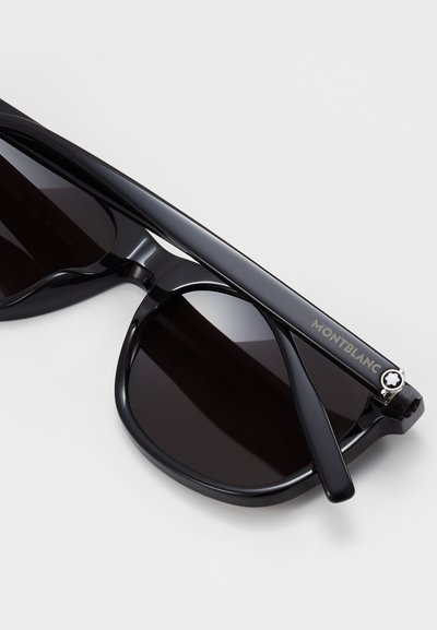 Schwarze Sonnenbrille mit dunklen Gläsern, einem glänzenden Rahmen und einem Montblanc-Logo an einem Bügel, das eine silberne Emblembekleidung am Schläfenbereich aufweist.