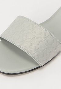 Sandale à glissière gris clair avec une bride en tissu texturé présentant un motif de logo subtil, ainsi qu'un footbed et une semelle extérieure lisses et mats.