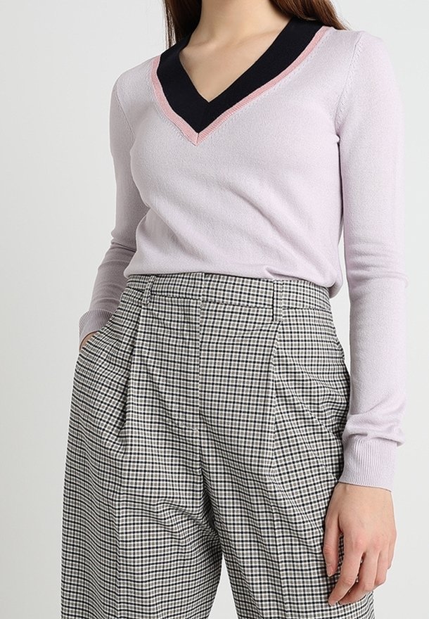 Helllila Pullover mit einem schwarz-pinken V-Ausschnitt, kombiniert mit hochgeschnittenen, karierten Hosen mit Faltendetails.
