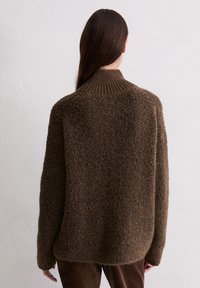 Brązowy, teksturowany sweter z wysokim kołnierzem, luźnym krojem i prążkowanymi detalami; wykonany z miękkiego, puszystego materiału.