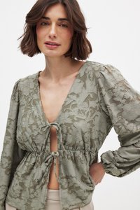 Ljusgrön blus med blommig spetsdesign, djup V-halsringning, knytning i midjan och puffärmar med elastiska manschetter.