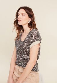 Zwart en beige top met korte mouwen en een bladpatroon, voorzien van een V-hals en gestructureerde metallic accenten op de mouwen.