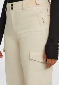 Beige cargo pants van gladde stof met twee voorzakken, knoopsluiting en een zijzak met een klep.