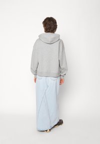 Sudadera gris con capucha y hombros caídos, combinada con una falda larga azul claro con costura central y bolsillos. Zapatillas negras.