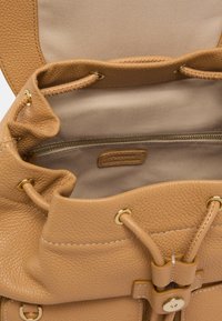 Borsa a secchiello in pelle color tan con finitura texturizzata, accessori in metallo dorato e fodera beige morbida. Presenta una chiusura con coulisse e una tasca interna.