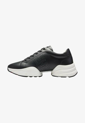 Basket en cuir noir avec motif géométrique perforé, lacets noirs et semelle blanche épaisse avec une bande de roulement texturée, vue de côté.