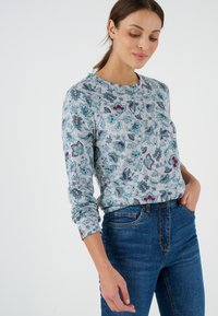 Camisa de manga larga gris claro con un patrón floral en tonos azul petróleo y burdeos, combinada con unos jeans de talle alto azul oscuro. Textura suave.